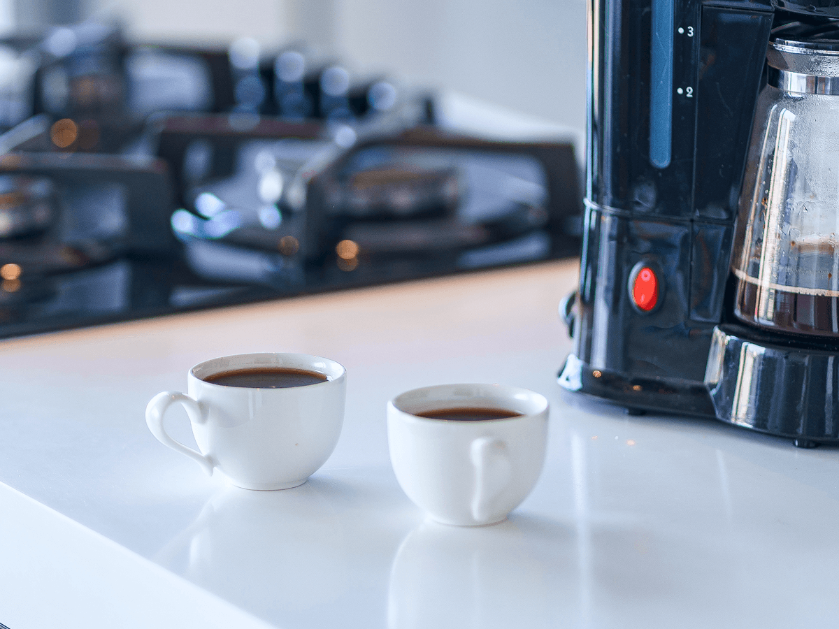 Two cups of brewed coffee on a kitchen counter next to a drip coffee maker