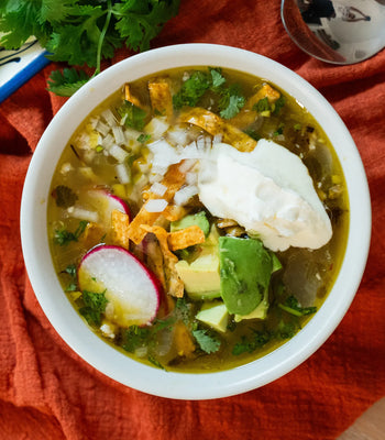 An overhead shot of a finished bowl of turkey soup, fully garnished with sour cream, avocado, and cilantro