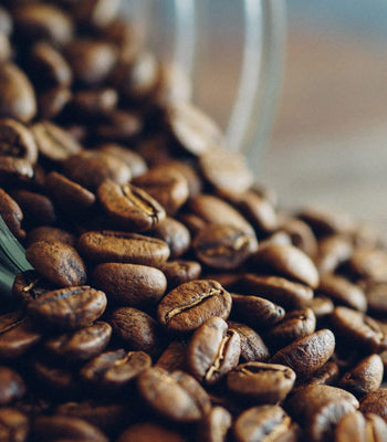 Roasted coffee beans spilling from a jar, symbolizing the natural source of caffeine in coffee