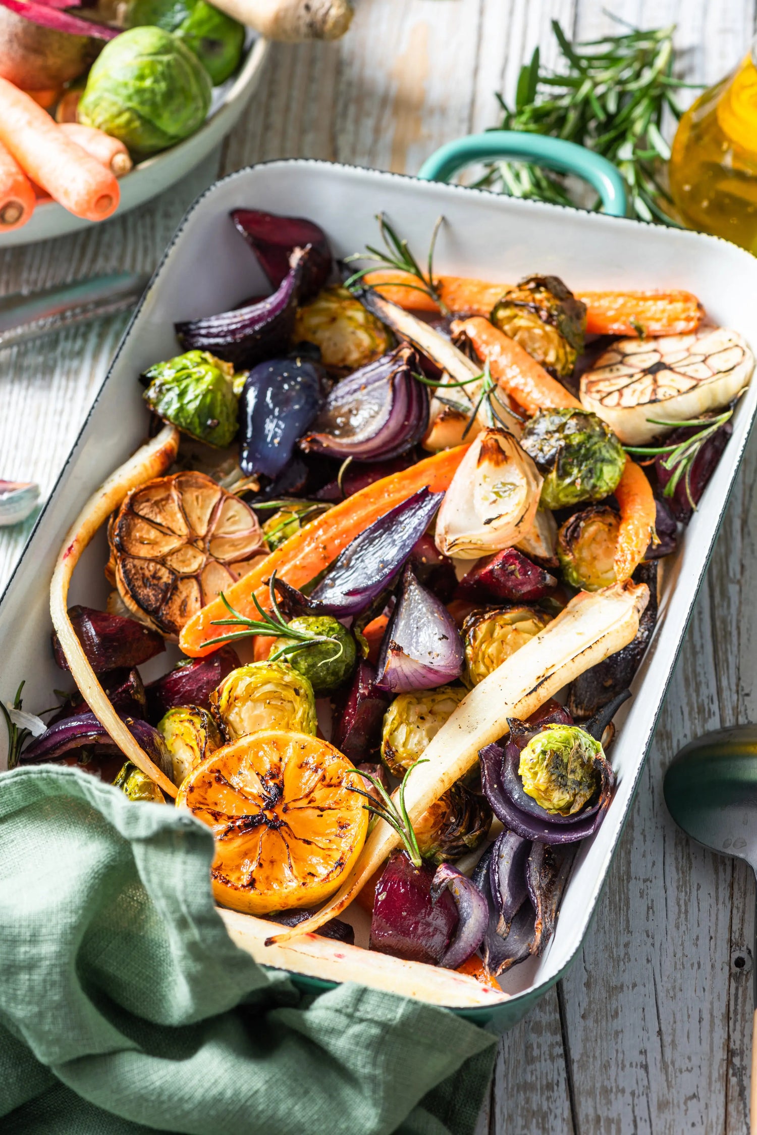 Roasted carrots, parsnips, onions, and Brussels sprouts in a white baking dish with rosemary
