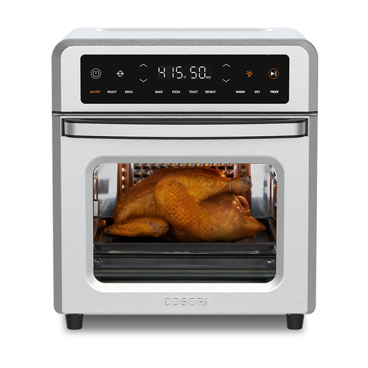 Cosori 13-Quart Air Fryer Oven with a whole roasted chicken cooking inside. Stainless steel finish